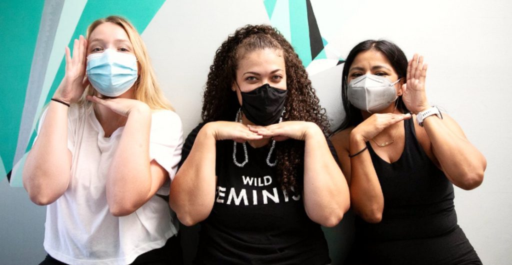 Grace, Mariah, and Carmen sitting in front of graphic wall at our Eagle Rock Studio