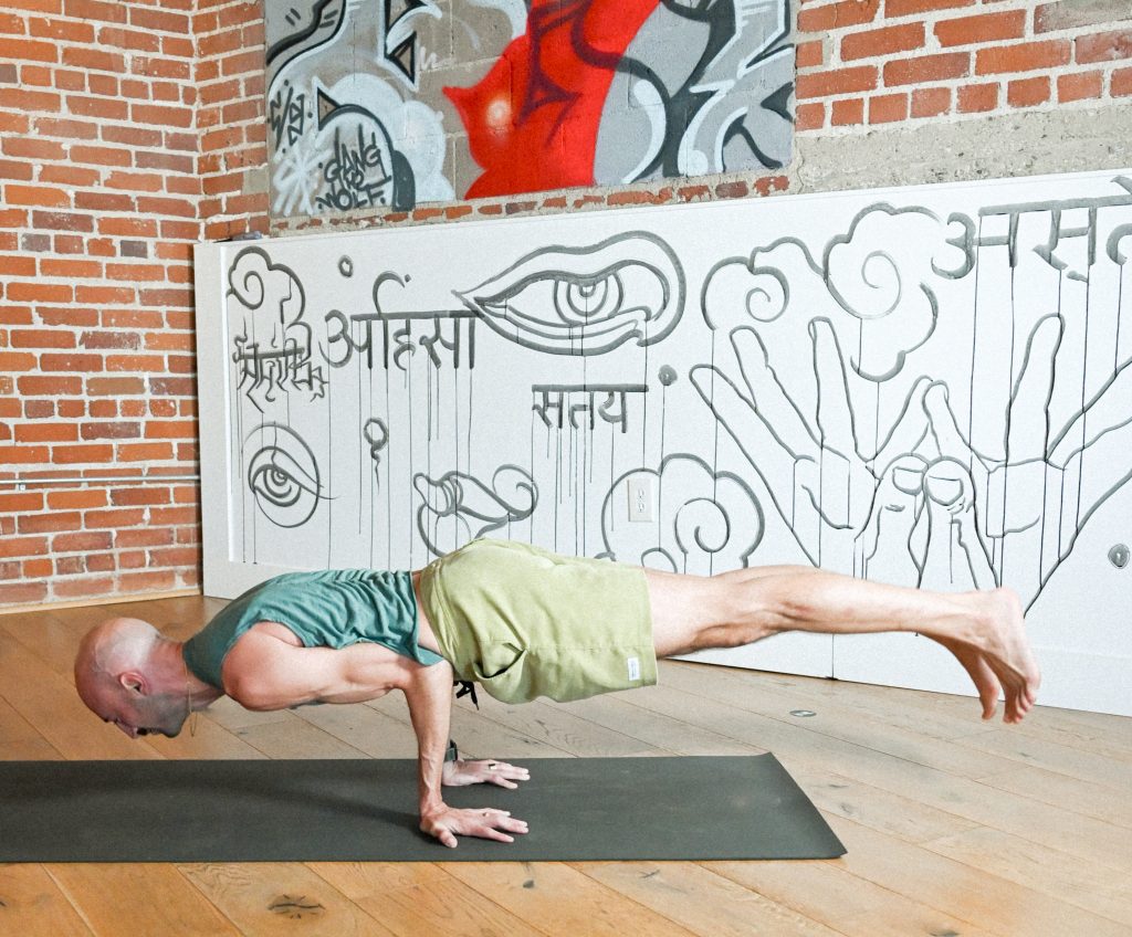 image of Nate Apuna, yoga teacher at One Down Dog Yoga and Fitness doing an arm balance on a yoga mat